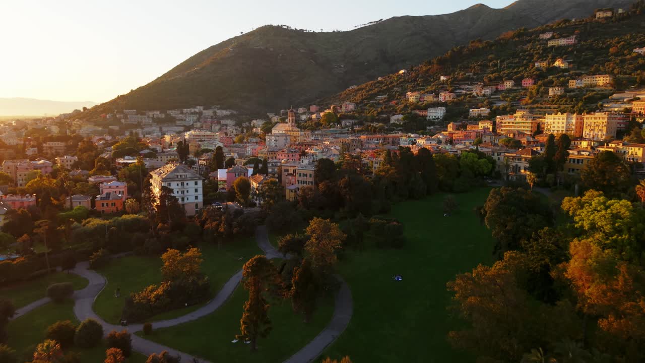 Genoa cityscape with sun setting behind mountains, parks, and buildings