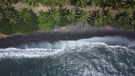 Geheime-Oase:-4K-Drohnenaufnahme-Von-Oben-Nach-Unten-Aus-Der-Luft-Eines-Einsamen-Mädchens,-Das-Am-Unberührten-Schwarzen-Sandstrand-In-Gretek,-Bali,-Liegt