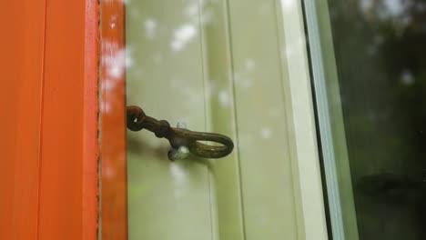 exterior view of an old window locking mechanism from outside, black painted old traditional wooden residential house, red window frame, overcast day, medium handheld closeup shot