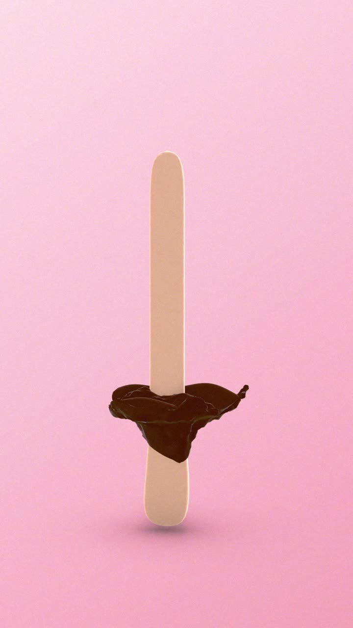 Cioccolato liquido che schizza attorno a un bastoncino di ghiacciolo su sfondo rosa