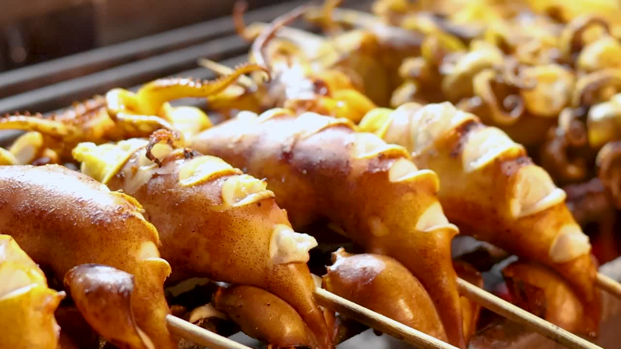 Un très gros plan serré sur des brochettes de calamars assaisonnées cuisant sur un grill à charbon chaud.