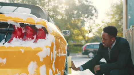 hombre lavando un coche amarillo en un lavado de coches al aire libre
