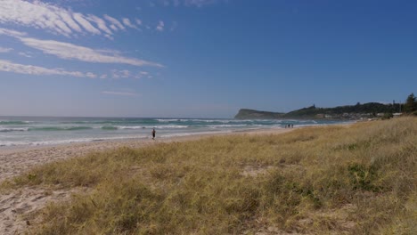 Hierba-Spinifex-Littoreus-En-Las-Dunas-De-Arena---Gente-Caminando-En-La-Playa-De-Lennox-Head-Con-Lennox-Point---Nueva-Gales-Del-Sur,-Australia