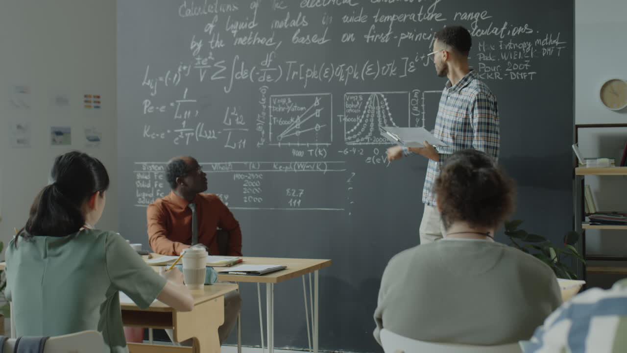 Teacher explaining complex scientific equations on a blackboard to students in a classroom