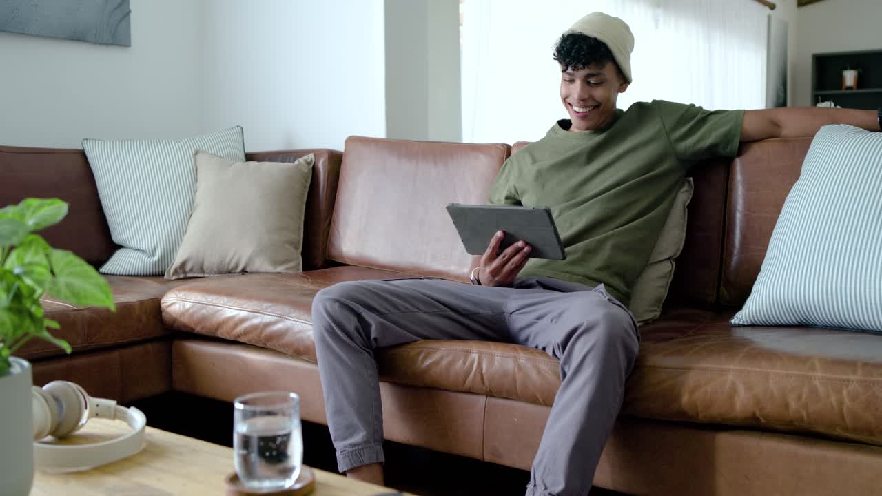 African American man sitting on brown sectional sofa, tapping tablet for entertainment, copy space