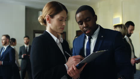 caucasian businesswoman holding documents and talking with an african american colleague discussing something in the hall at the meeting