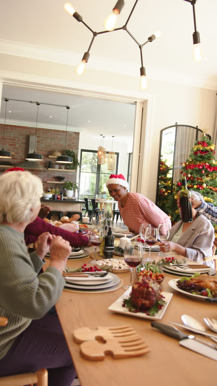 Vertical video of happy diverse senior friends at christmas dinner table, copy space, slow motion
