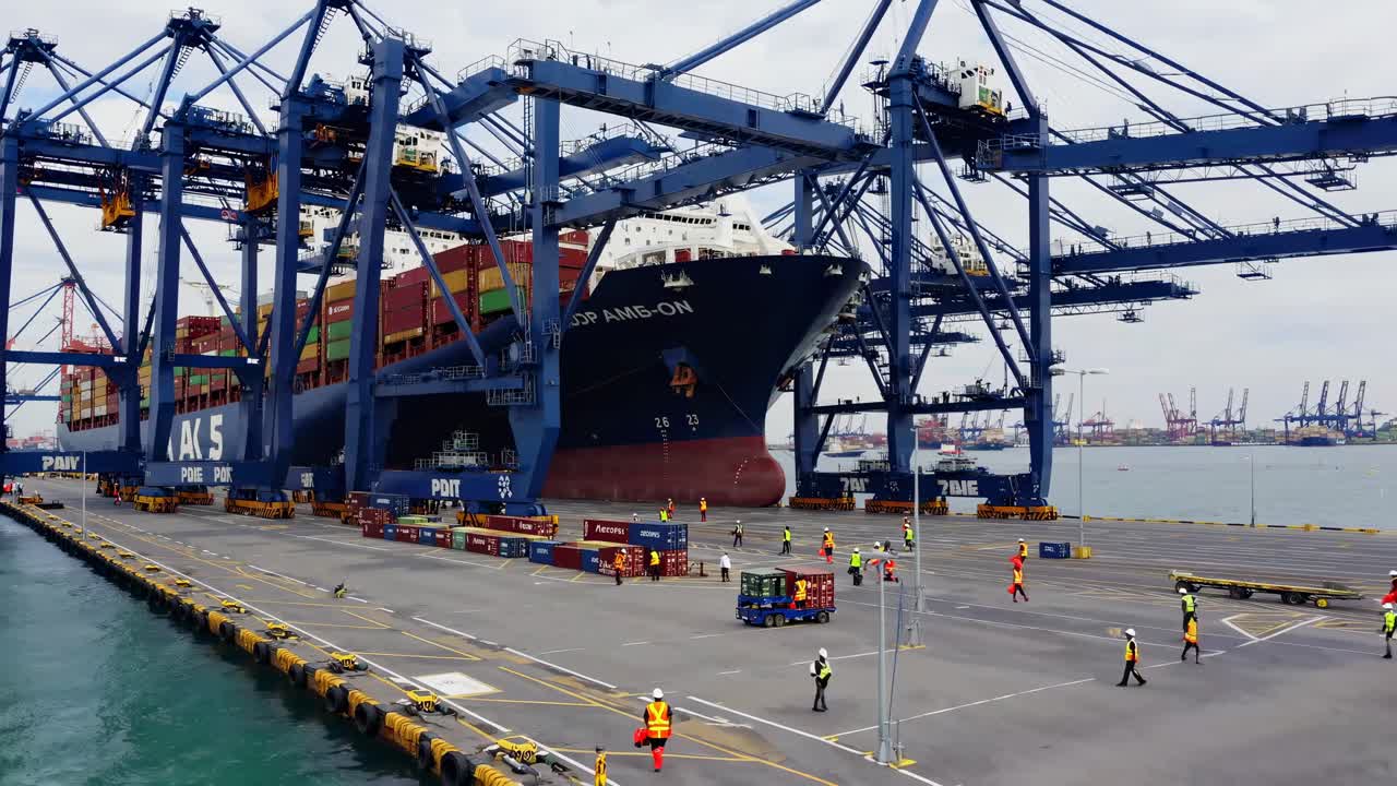 High-angle video shot of a bustling port with cranes unloading a cargo ship, capturing the dynamic