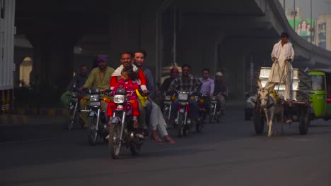 a close up fast forward shot of the traffic under the fly over, passing motor bikes and cars, buses, rickshaw`s, a donkey car is going on the road too