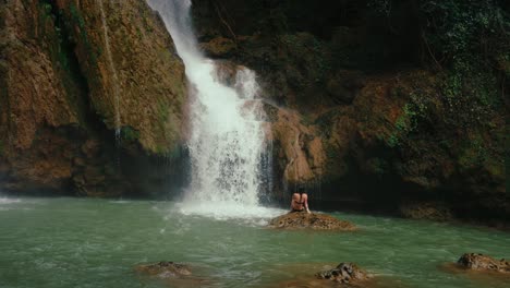 rear shot of a person sitting on a rock, facing the waterfall, creating a reflective, poetic visual ideal for themes of solitude or awe.