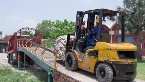 forklift loading cotton bales onto truck at a factory