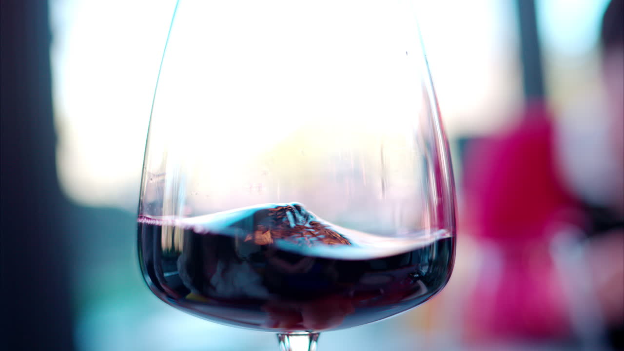 Red wine being swirled around in a glass with blurred people on the background
