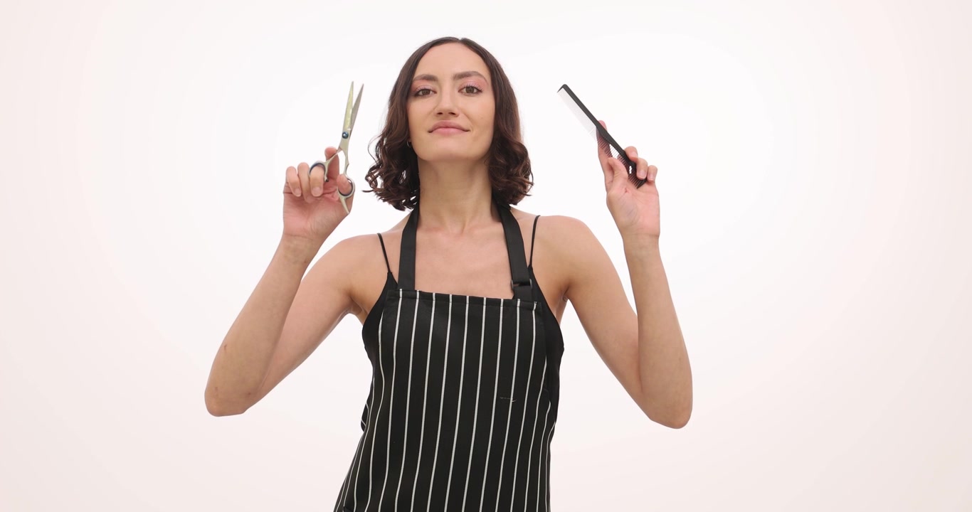 Woman hairdresser smiles holding comb and pair of scissors