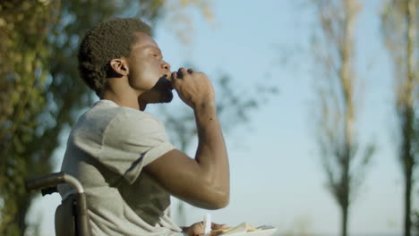 side view shot of young man in wheelchair enjoying his snack