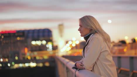 Una-Mujer-Joven-Se-Para-En-Un-Puente-En-Una-Ciudad-Nocturna-Y-Mira-Pensativamente-A-Lo-Lejos