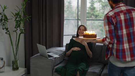 생일 케이크와  ⁇ 불을 가진 남자가 임산부에게 그녀의 생일을 축하하고 있습니다.