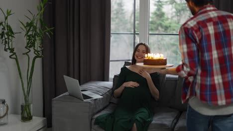 a man with birthday cake and candle giving it to pregnant woman celebrating her birthday