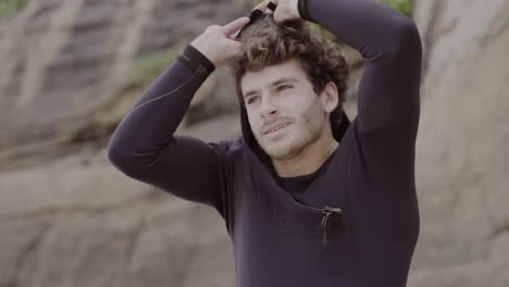 a man puts on his wetsuit with a hood, preparing for a water sport