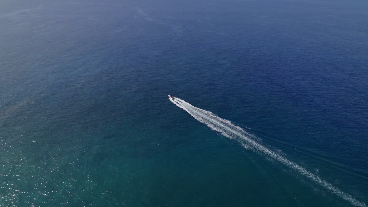 Motoscafo solitario sfreccia sull'acqua blu, ripresa di inseguimento con drone dall'alto.
