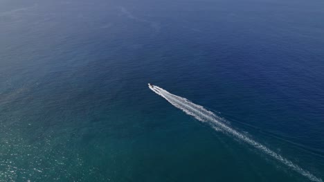 lone motor boat speeds across blue water, high angle drone tracking shot