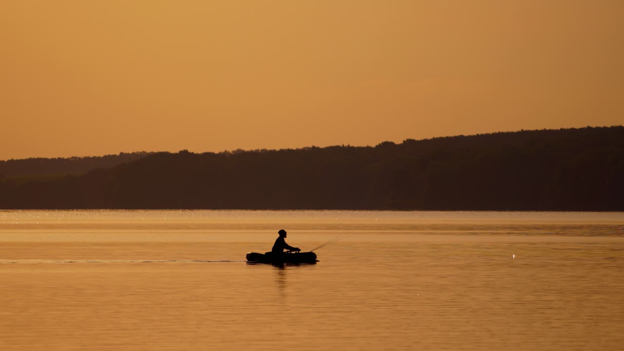 Silhouette of fisherman in boat. Fishing on a lake from the boat at sunset