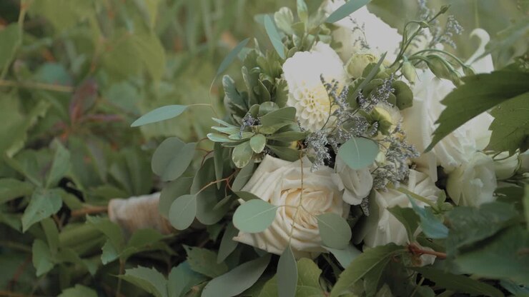 Bride picking up her beautiful white rose and lily bouquet of flowers off of a hedge of plants in the back yard