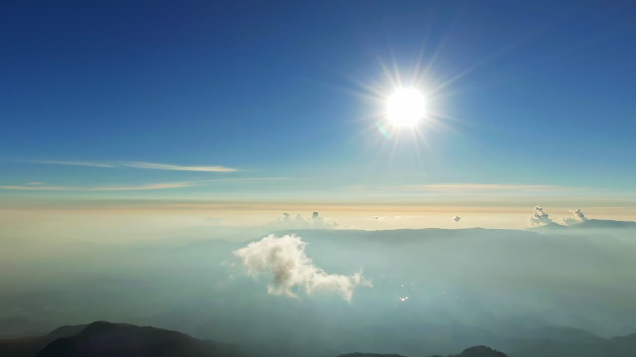 Colima Volcano crater with faint smoke plume rising above the cone to bright morning skyline with sun and drifting clouds over a misty valley