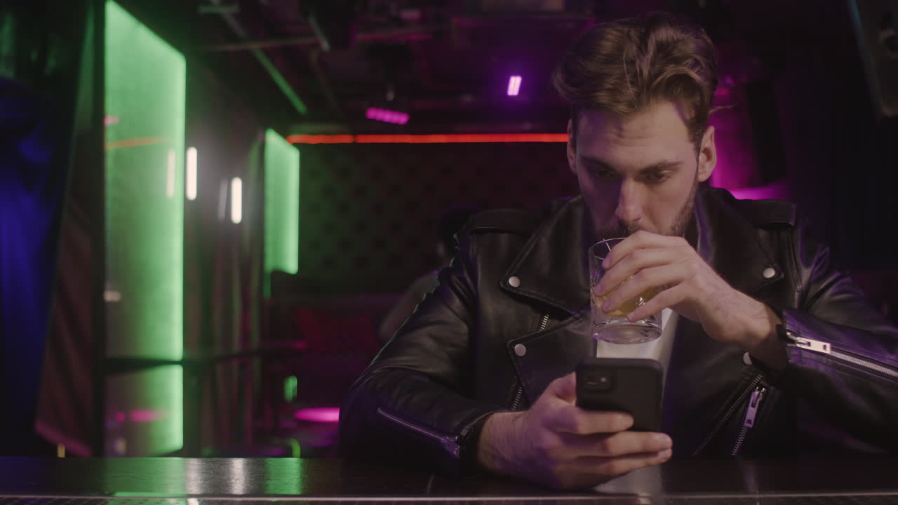 Uomo barbuto serio che beve e usa il telefono cellulare seduto al bancone del bar
