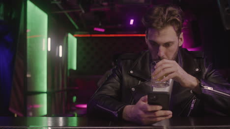 serious bearded man drinking and using mobile phone while sitting at bar counter