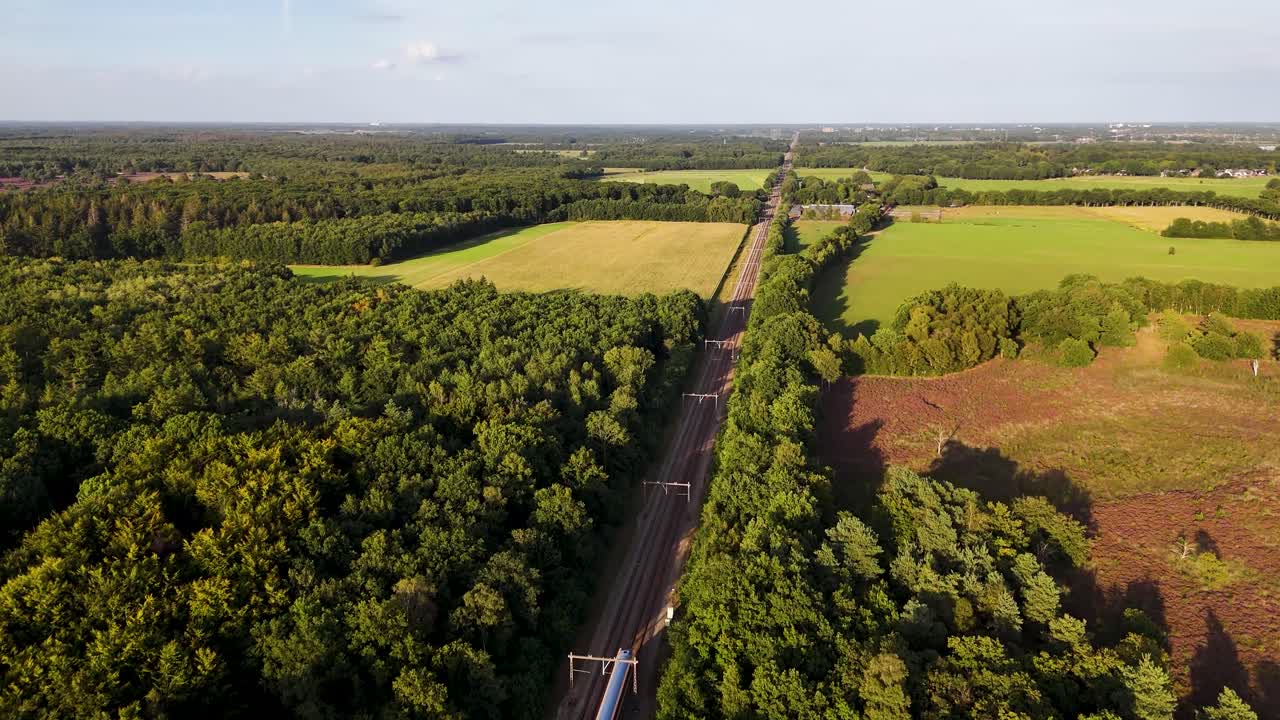 Aerial view of train tracks through forest and fields