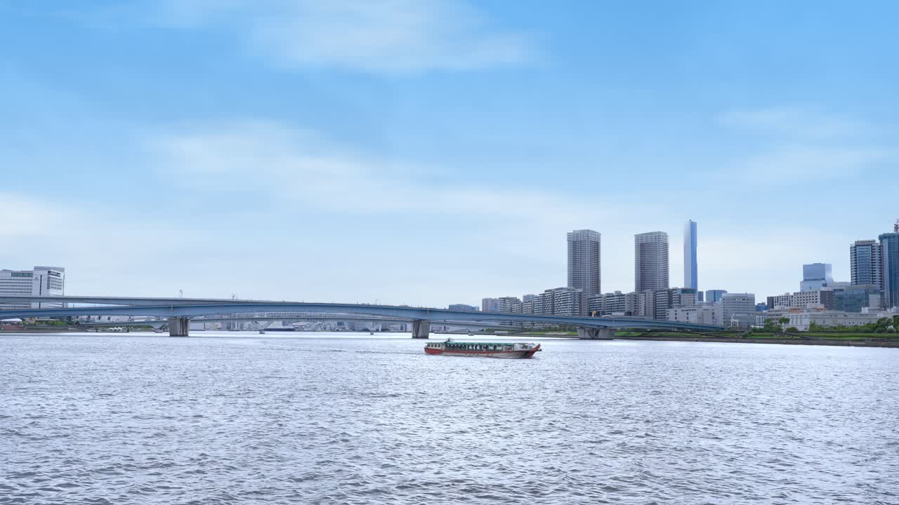 A peaceful wide shot of a boat traveling on Tokyo Bay with a large bridge and the cityscape in the background