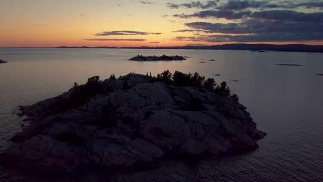 rocky pine tree island in big lake just after sunset, drone aerial wide orbit pan