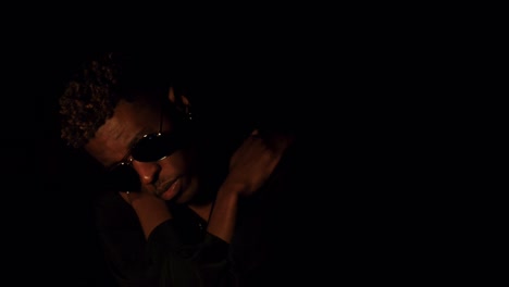black man with bleached hair and sunglasses hugging himself in dark