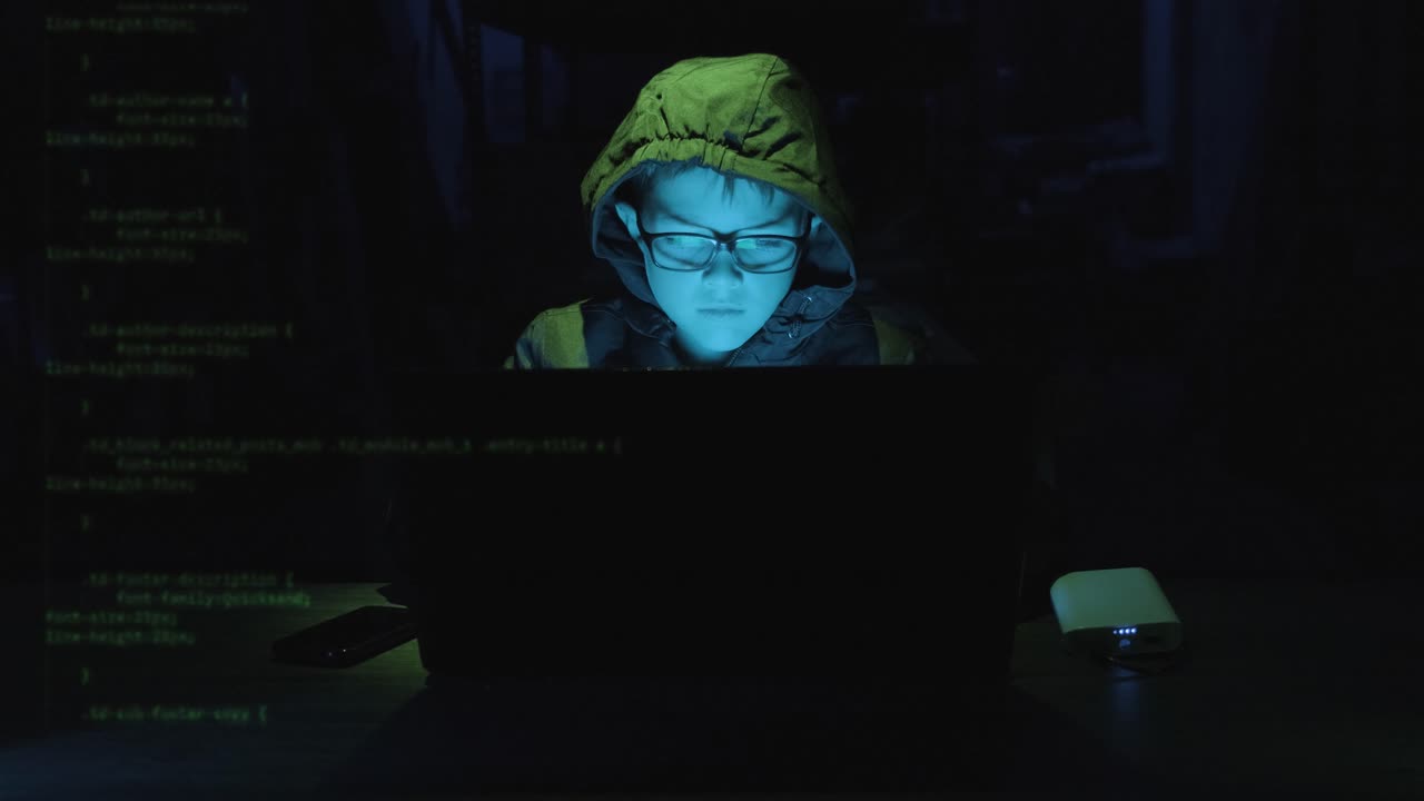Young Boy Hacker Typing On Laptop With Security Codes Moving In The Screen In A Dark Workplace. - static