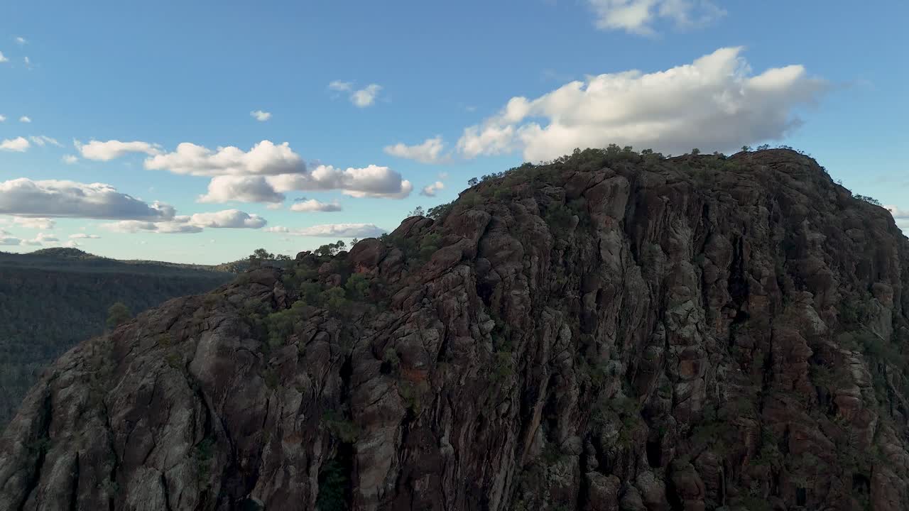 Un filmato drone panoramico si estende sull'aspra Timor Rock, rivelando scogliere spettacolari, pendii boscosi e un cielo vasto sotto la morbida luce del sole serale a Coonabarabran, Australia