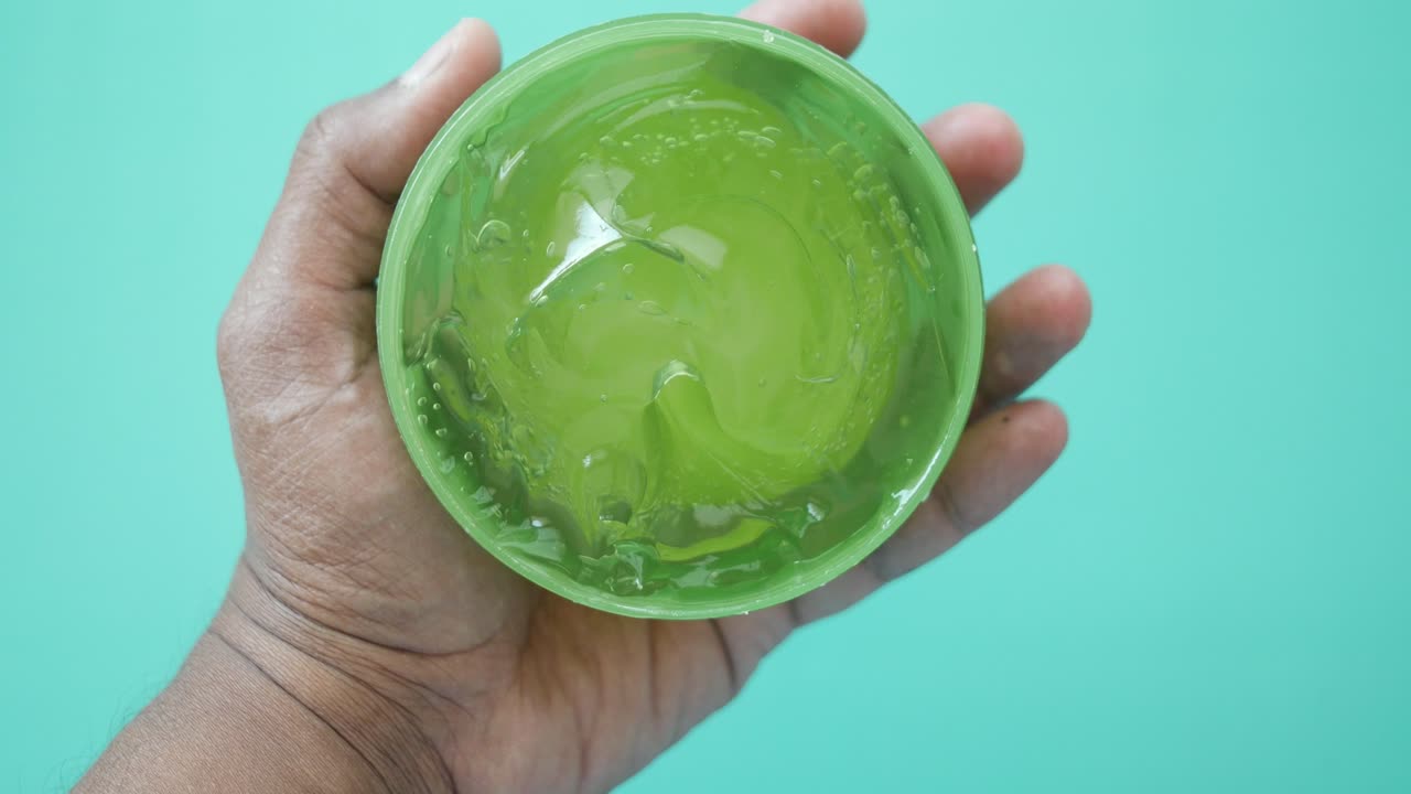 Primo piano della mano di una persona che tiene un contenitore di gel di aloe vera
