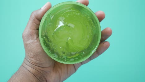 close-up of a person's hand holding a container of aloe vera gel