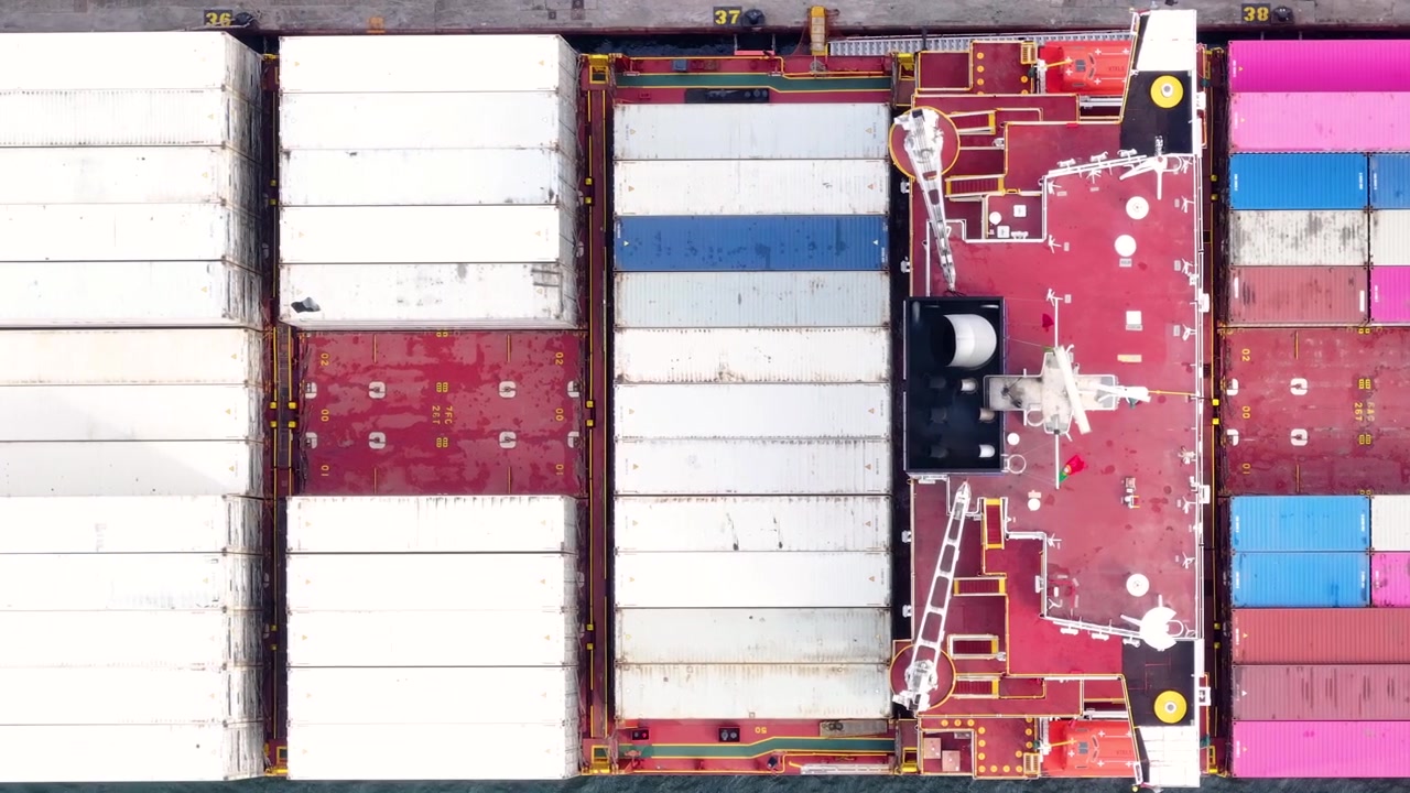 Farverige shippingcontainere fylder dækkene på et stort containerskib, mens det lægger til kaj ved en travl fragtterminal. Dette indblik i maritim logistik fremhæver vigtige globale handelsaktiviteter.