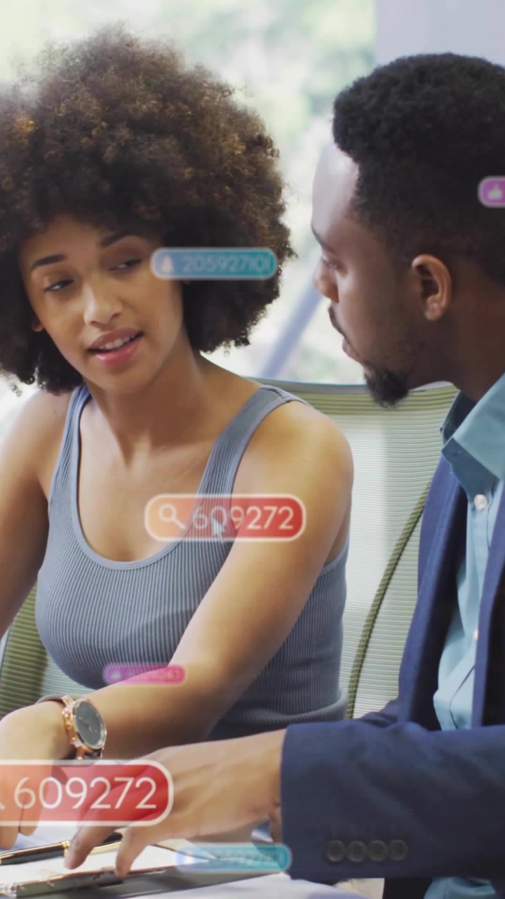 Video verticale: Donna che indica documenti mentre un uomo clicca il mouse, esaminando i dati aziendali, con badge sui documenti.