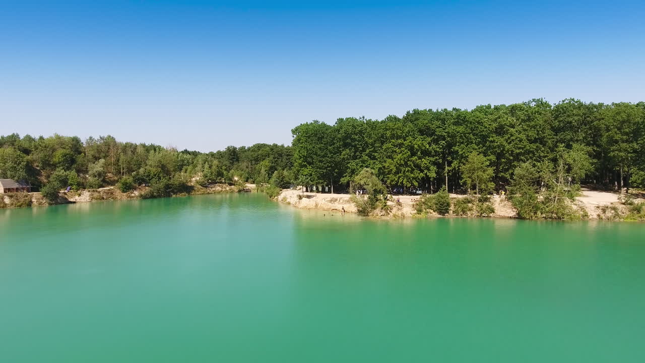 Blue sky reflecting in water. Gradual approaching to the waterfront covered with thick forests. Aerial view.
