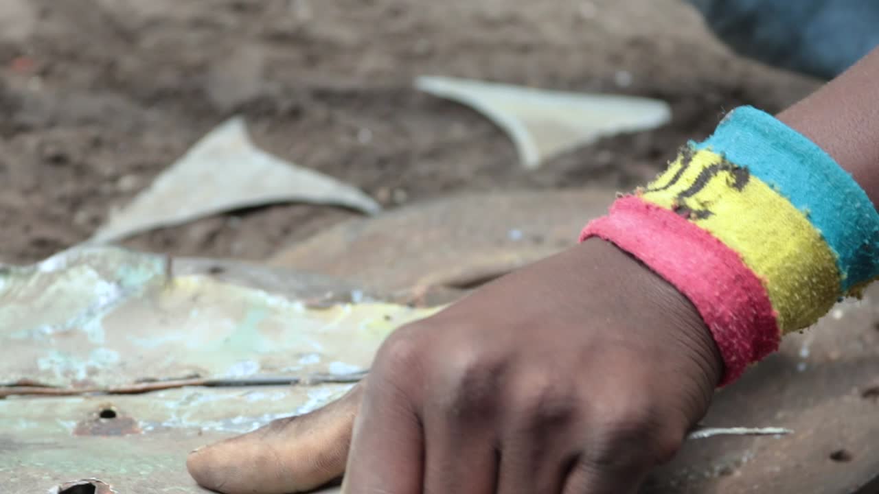Low angle shot of a Congolese teenager straightening a car part for charcoal stove production.