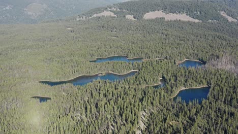 Slow-motion-Top-view-of-the-clear-sky-Lakes-wilderness,-small-lakes-in-between-the-wilderness-of-a-forest-in-a-mild-cold-climate-in-a-natural-background