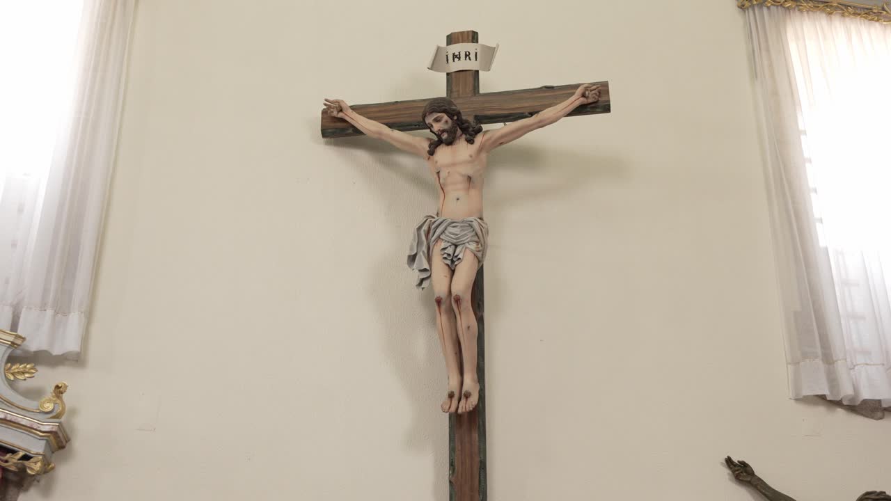 wooden crucifix depicting Jesus Christ, mounted on a white wall inside a well-lit church