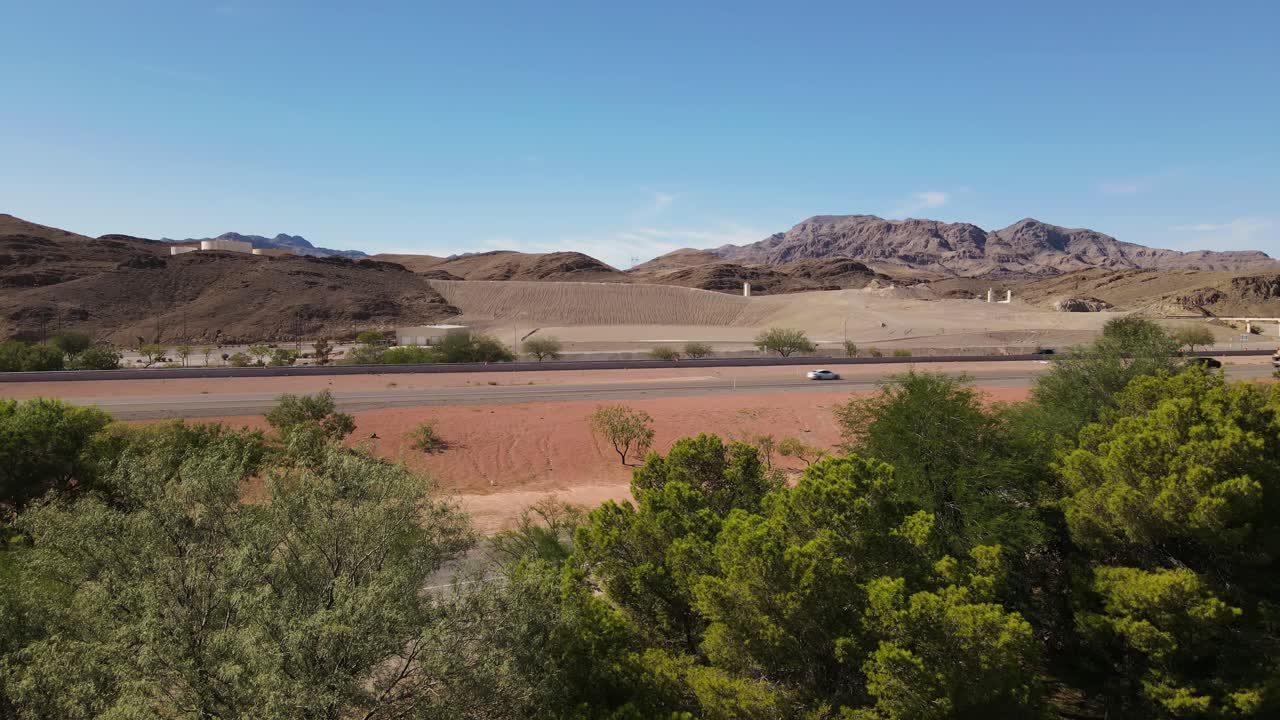전경에 나무가 있고 푸른 하늘과 산이 배경에 있는 사막의 고속도로 측면