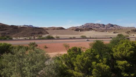 vista lateral de la carretera en el desierto con árboles en primer plano, cielos azules y montañas en segundo plano