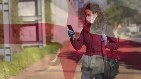 english flag waving against woman wearing face mask using smartphone