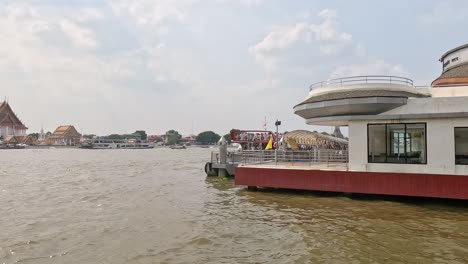 a boat passes a modern riverfront building in bangkok. the scene captures the bustling river life under bright daylight