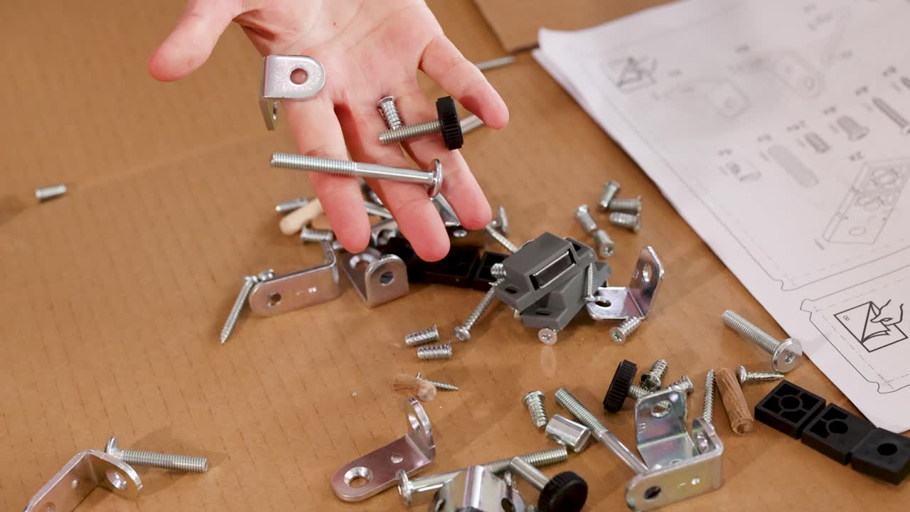 Hands sorting and assembling furniture hardware on a table with instructions in a well-lit environment