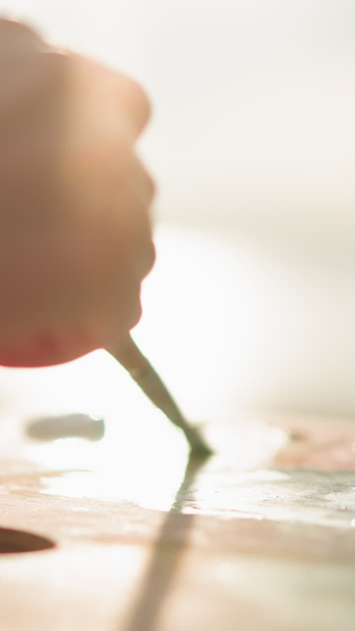 한 여성의 손이 으로 장식되어 있으며, 그녀는 부드러운 빛 아래 질로 패에 색을 혼합하는 장면입니다. 이 장면은 페인트를 혼합하는 섬세하고 집중된 과정을 강조합니다.