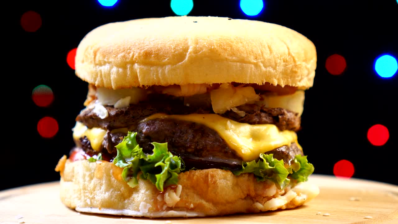 Cool beautiful fresh juicy cooked burger rotate on turntable against a background of colorful blurry lights.